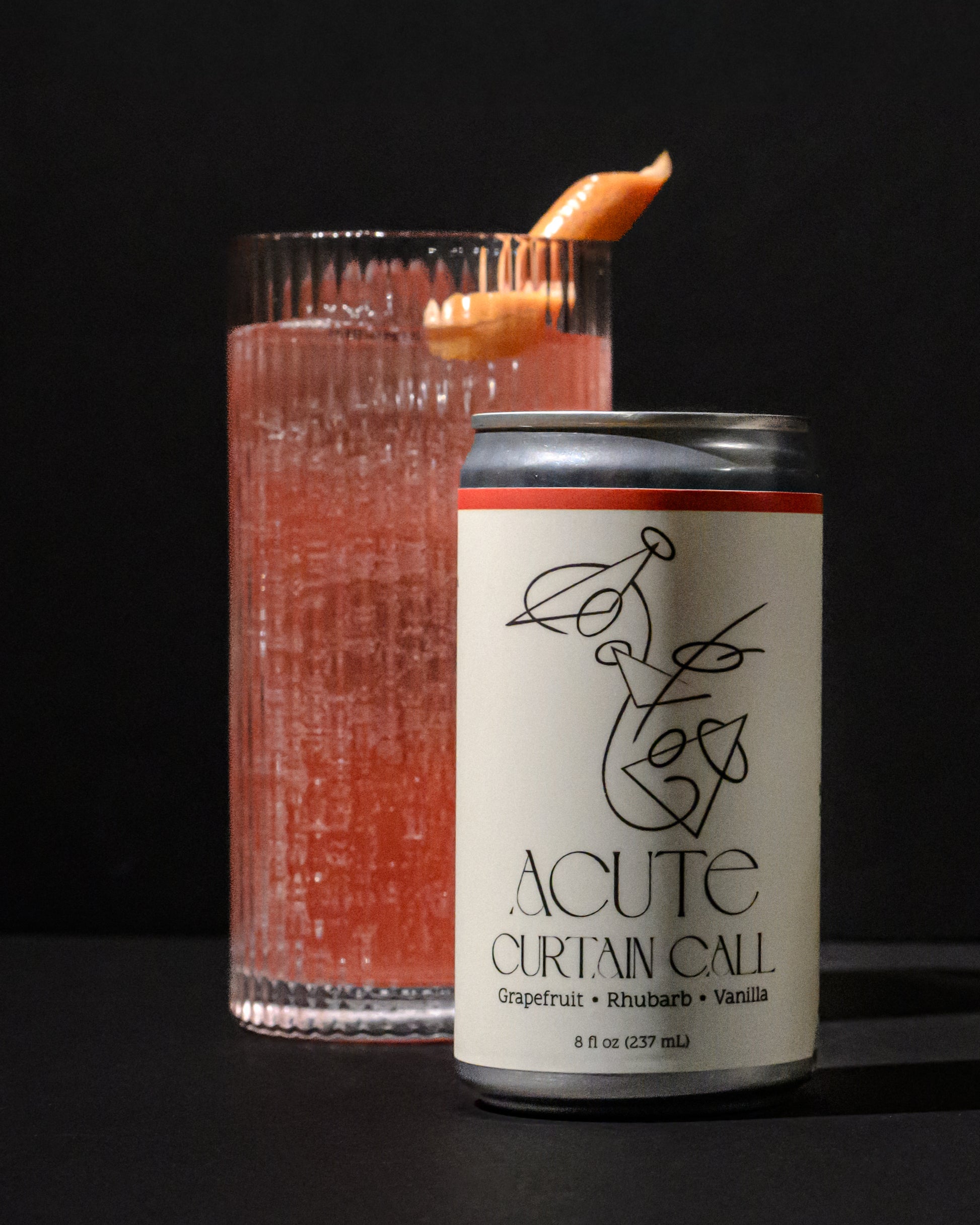 Canned drink labeled 'Acute' next to a glass with a red beverage on a dark background