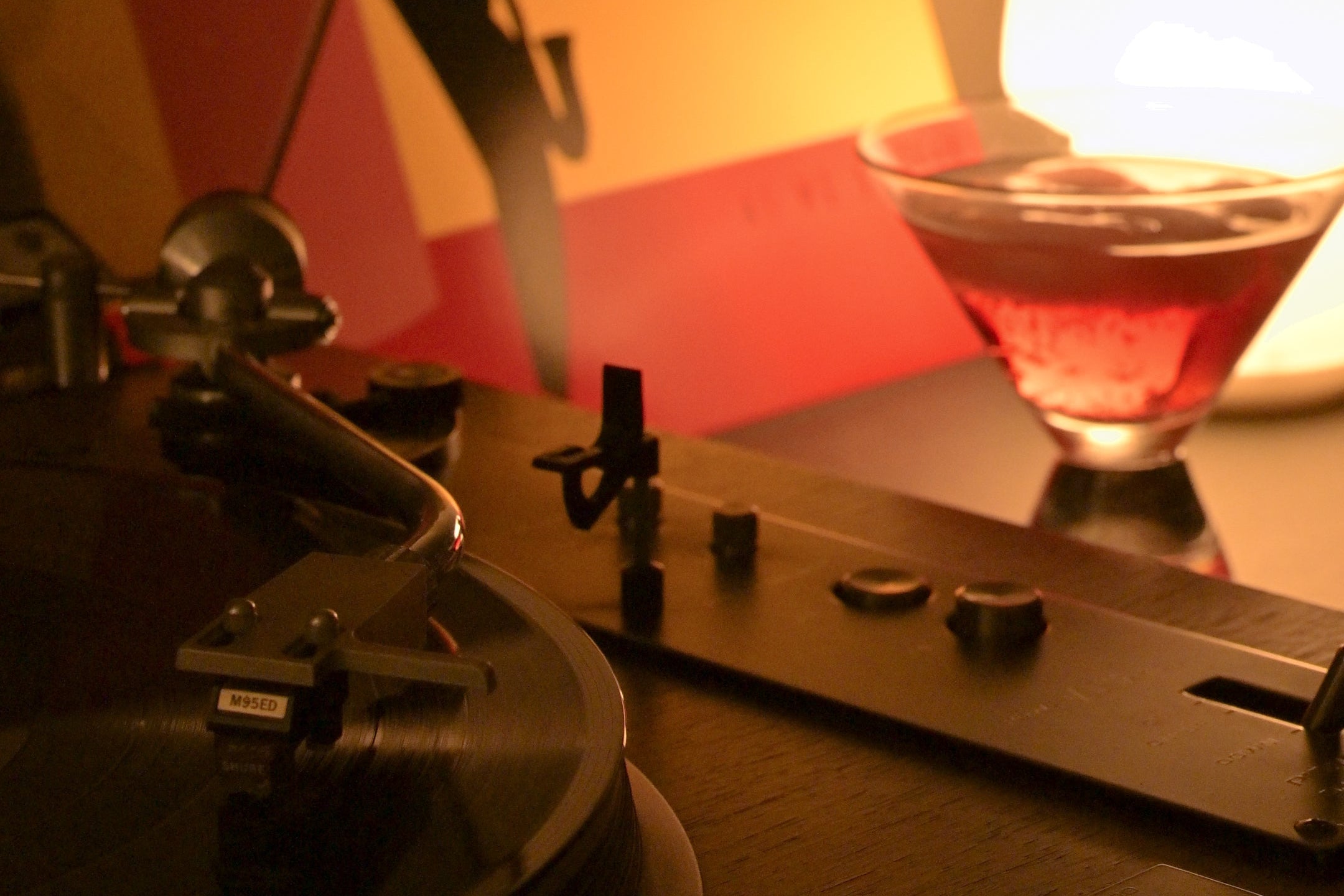Turntable with a record and a glass of velvet state on a wooden surface, with a warm light in the background.
