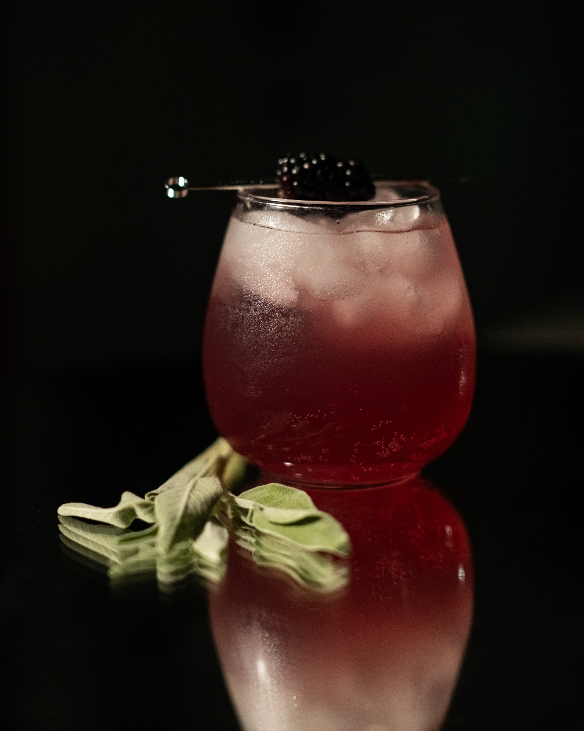 Pink cocktail in a glass with a blackberry on a dark background