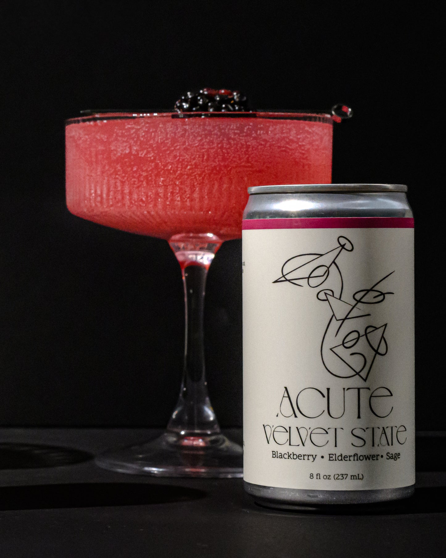 Red cocktail in a glass with a can of 'Acute Velvet State' on a black background